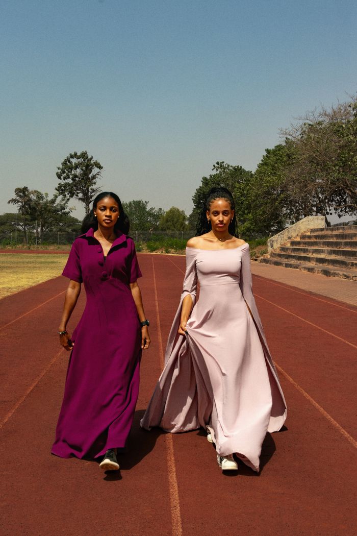 Two women elegantly dressed walking on an outdoor track amidst nature, showcasing fashion in motion.