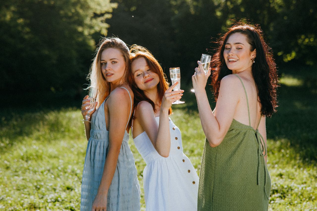 Three women in colorful dresses enjoy a sunny day with champagne in hand.